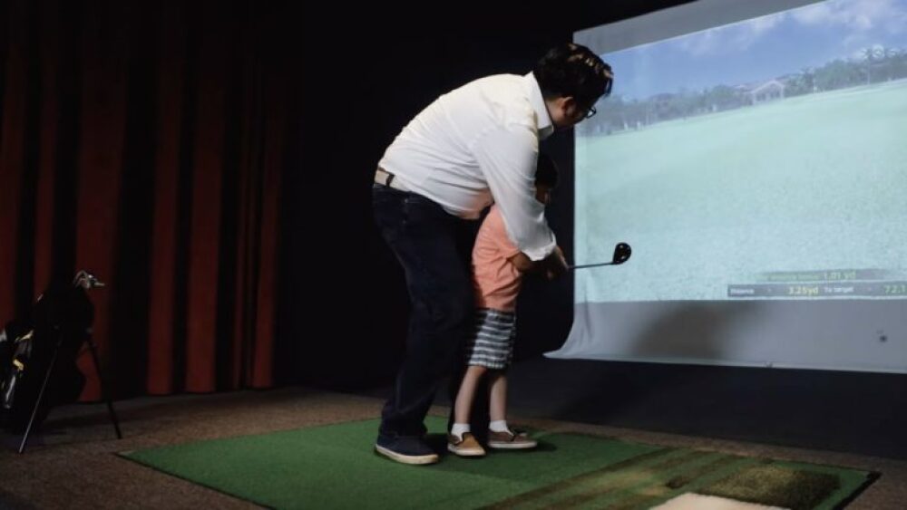 Adult Helping Child Swing Golf Club on Golfzon Golf Simulator