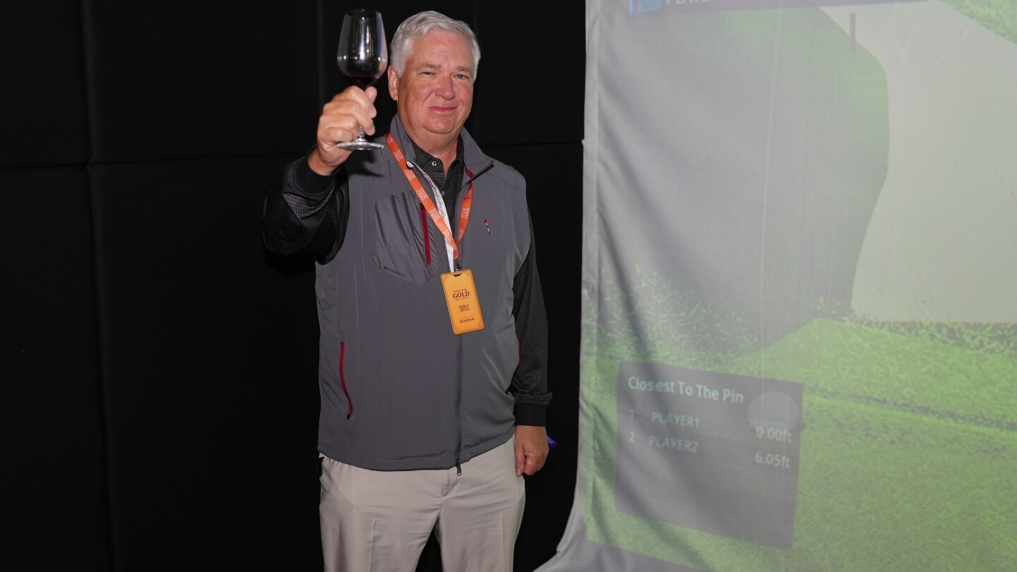 Mitch holding up a wine glass in front of a GOLFZON simulator after making a hole-in-one