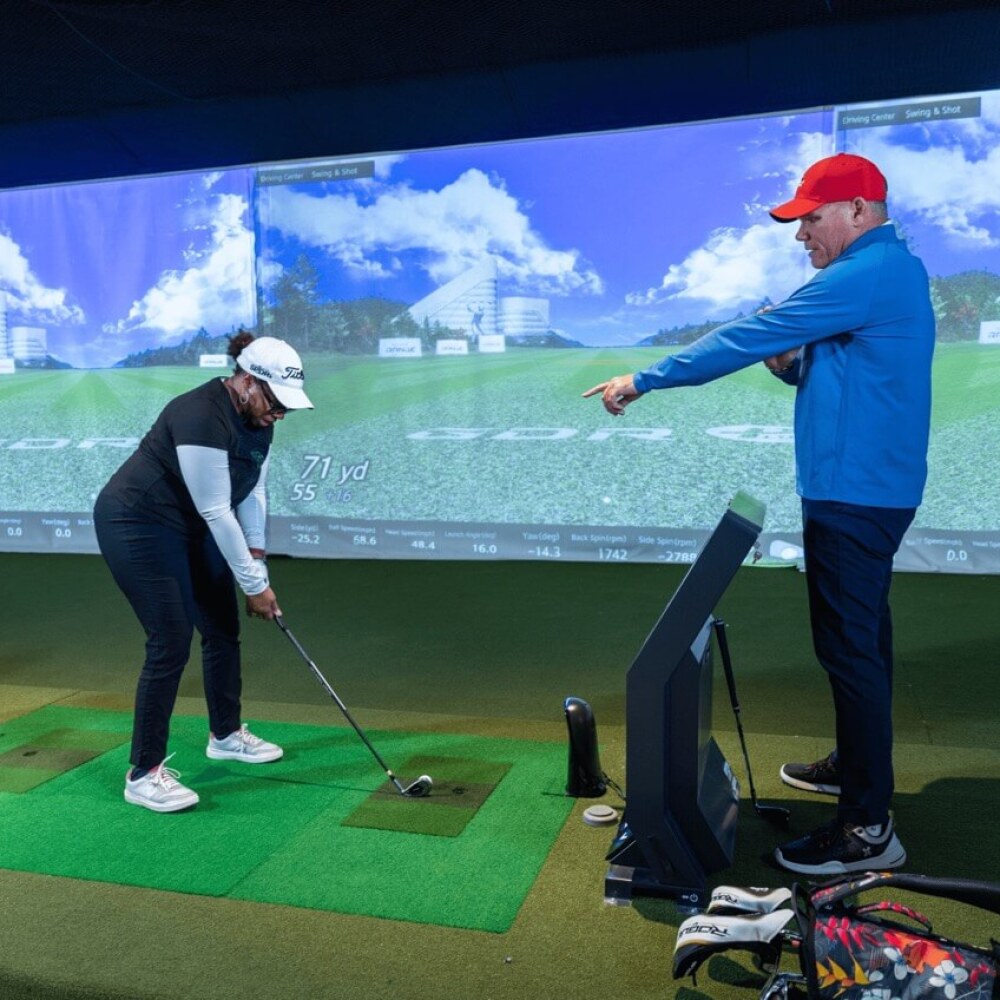 Instructor Working with Golfer Holding Wedge on GDR Golfzon Golf Simulator