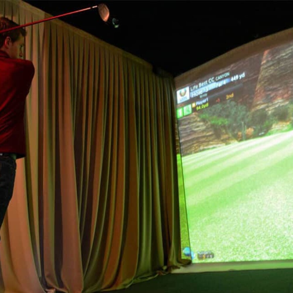 Behind Male Golfer Swinging On Golfzon Simulator with Curtain and Projector Screen
