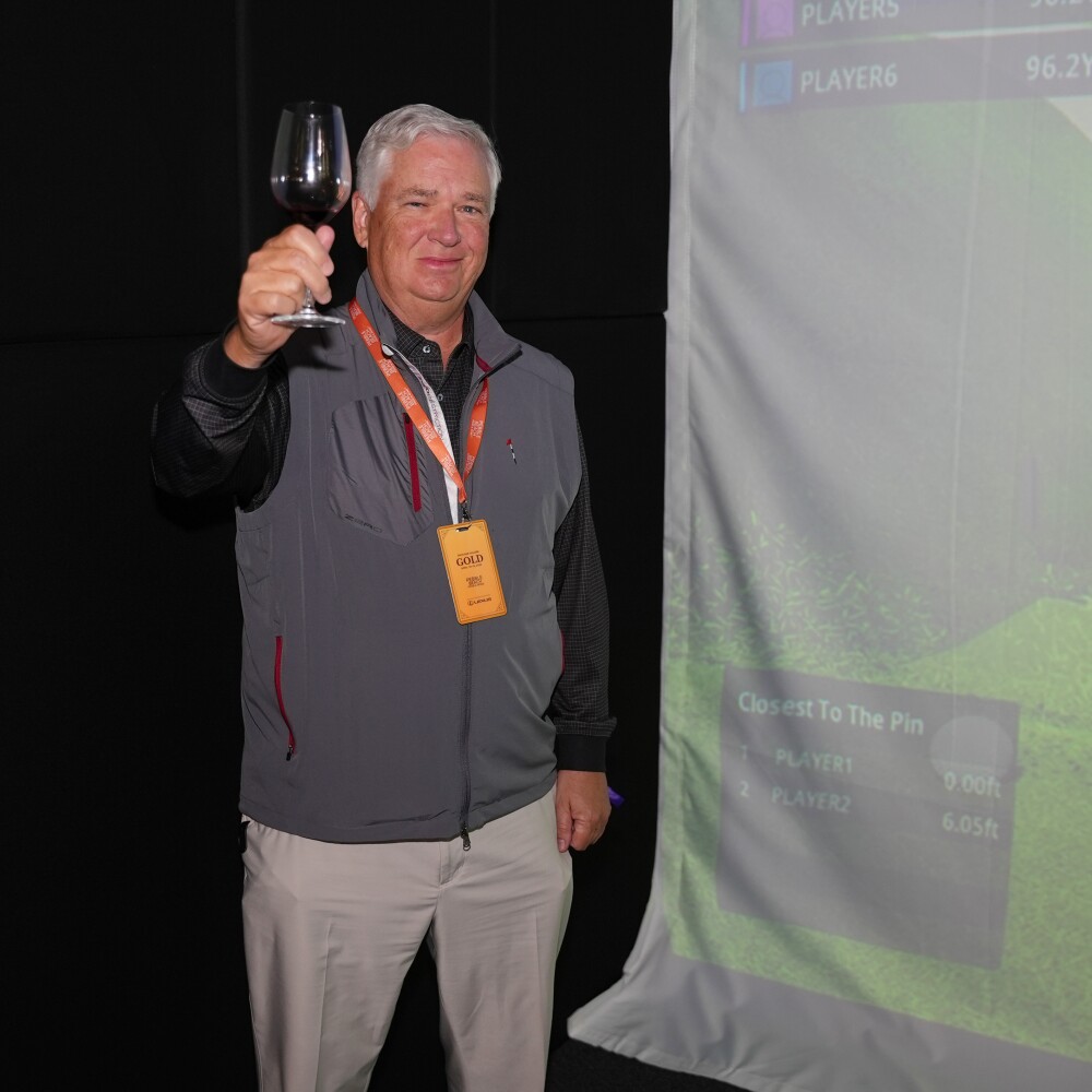 Mitch holding up a wine glass in front of a GOLFZON simulator after making a hole-in-one