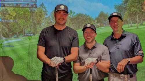 GOLFZON Tour Seeding Rounds - Week Two - Three Team Members with Golf Clubs Smiling in Front of GOLFZON TwoVision Simulator Screen