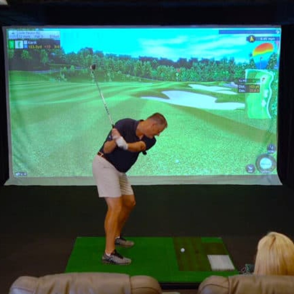 Male Golfer Swinging on Golfzon Residential Home Simulator Golfzon, Spectator in Theatre Seat Behind