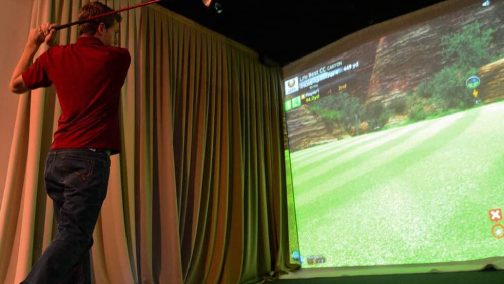 Behind Male Golfer Swinging On Golfzon Simulator with Curtain and Projector Screen